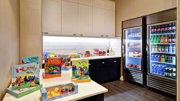 Una zona de cocina con mostrador que exhibe libros y juguetes infantiles, y dos refrigeradores llenos de bebidas.
