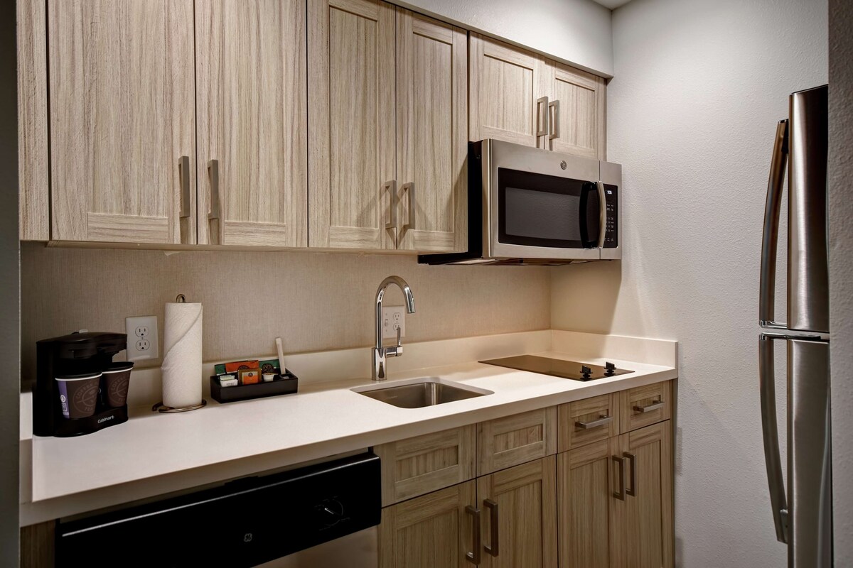 A modern kitchen with light wood cabinets, a stainless steel sink, a built-in microwave, and a refrigerator.