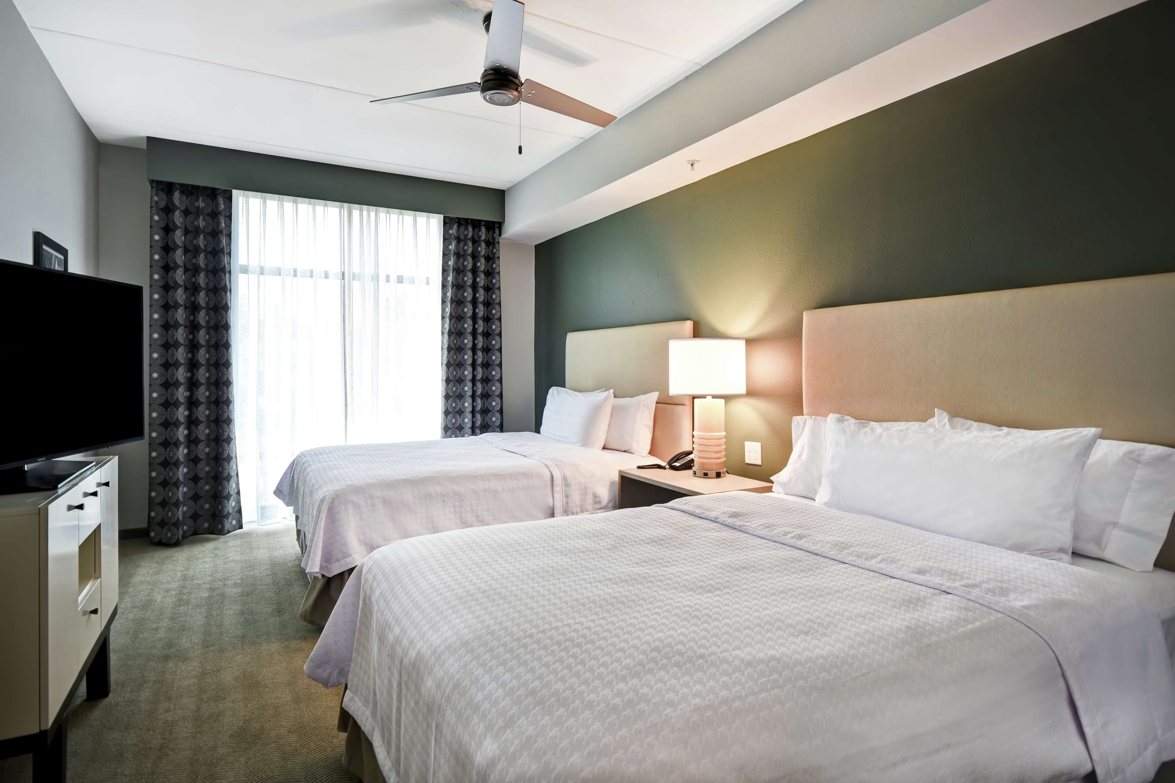 A hotel room with two beds, a TV, a desk, and a ceiling fan.