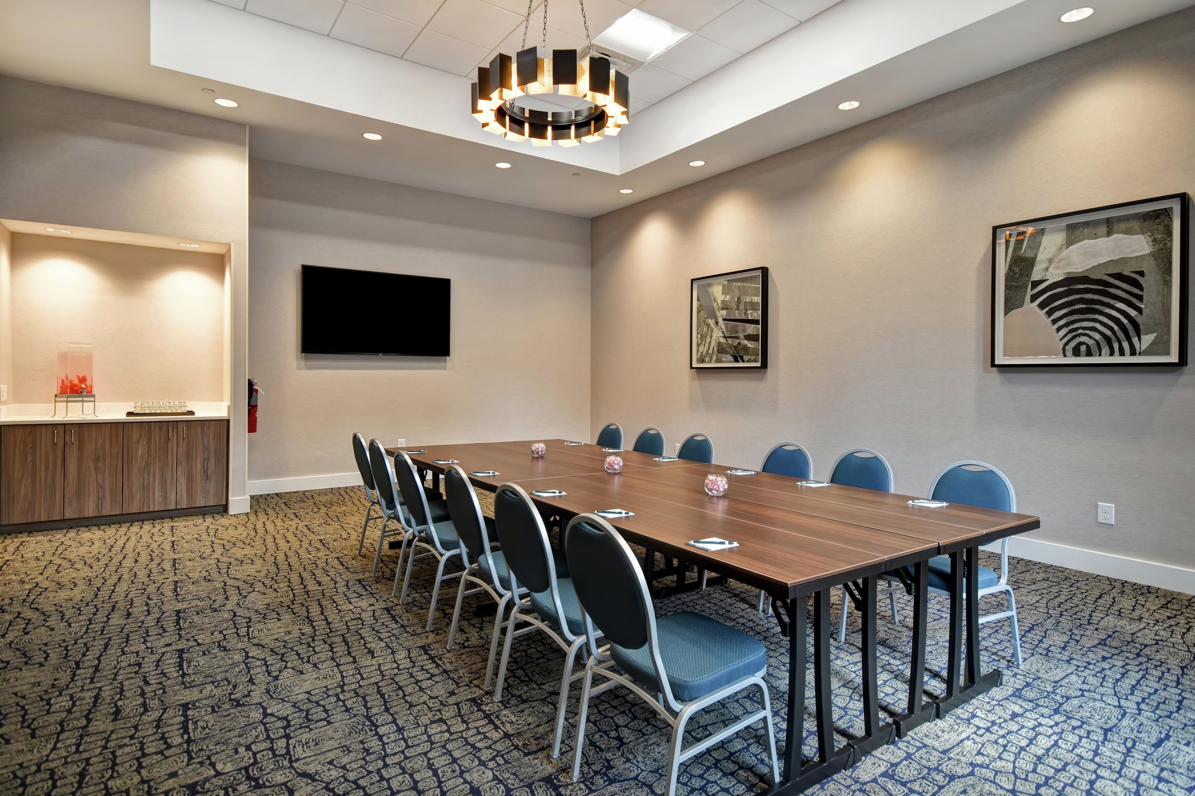 A conference room with a long table, chairs, a flat-screen TV, and artwork on the walls.