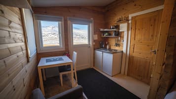 A compact cabin with a wooden interior, a small kitchenette, a dining area, and a view of a snowy landscape through the windows.