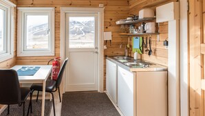 Une cuisine compacte équipée d’un évier, d’une cuisinière et de placards, un coin repas avec une table et des chaises, et une porte donnant sur une vue sur les montagnes.