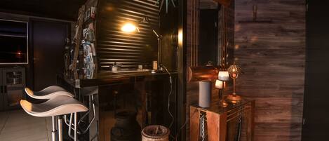 A bar area with stools, a wooden cabinet, and a rustic decor including a large pot and a clock.
