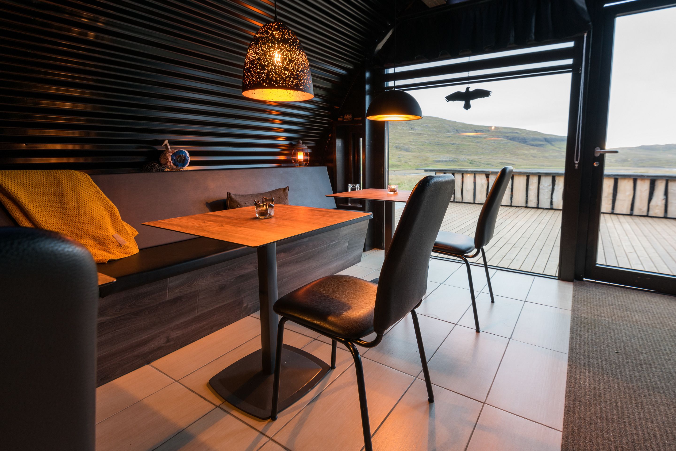 A modern interior with a wooden table and chairs, a bench with a yellow throw, and a view of the outdoors.