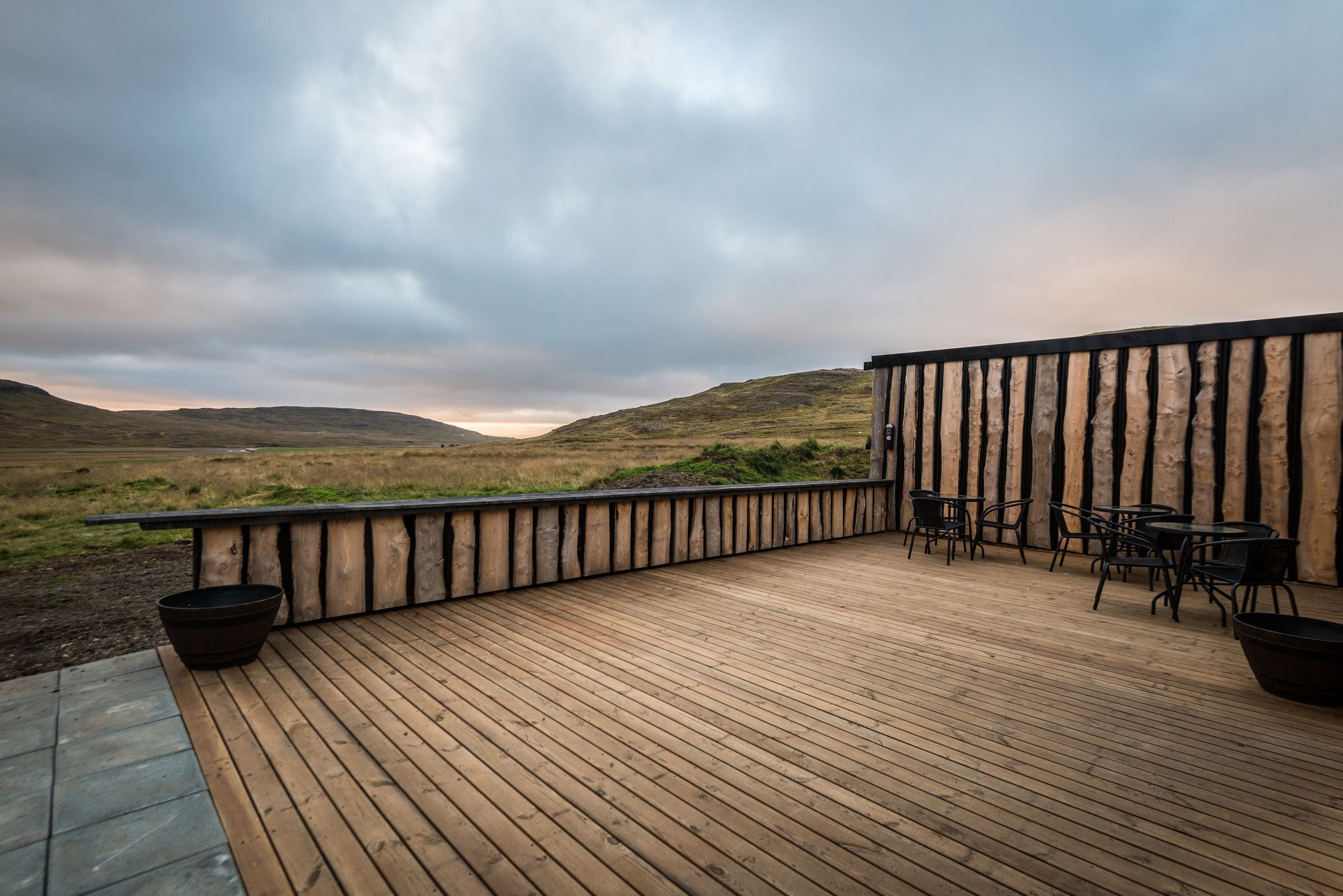 A wooden deck with outdoor seating, overlooking a grassy landscape and hills.