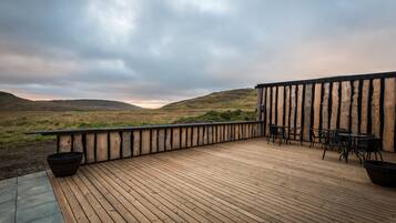 A wooden deck with outdoor seating, overlooking a grassy landscape and hills.