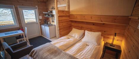 Une chambre dans une cabane en bois, avec un lit, une table de chevet et un bureau avec une chaise.