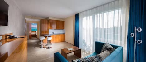 Habitación de hotel moderna con sala de estar, cocina y balcón con vistas.