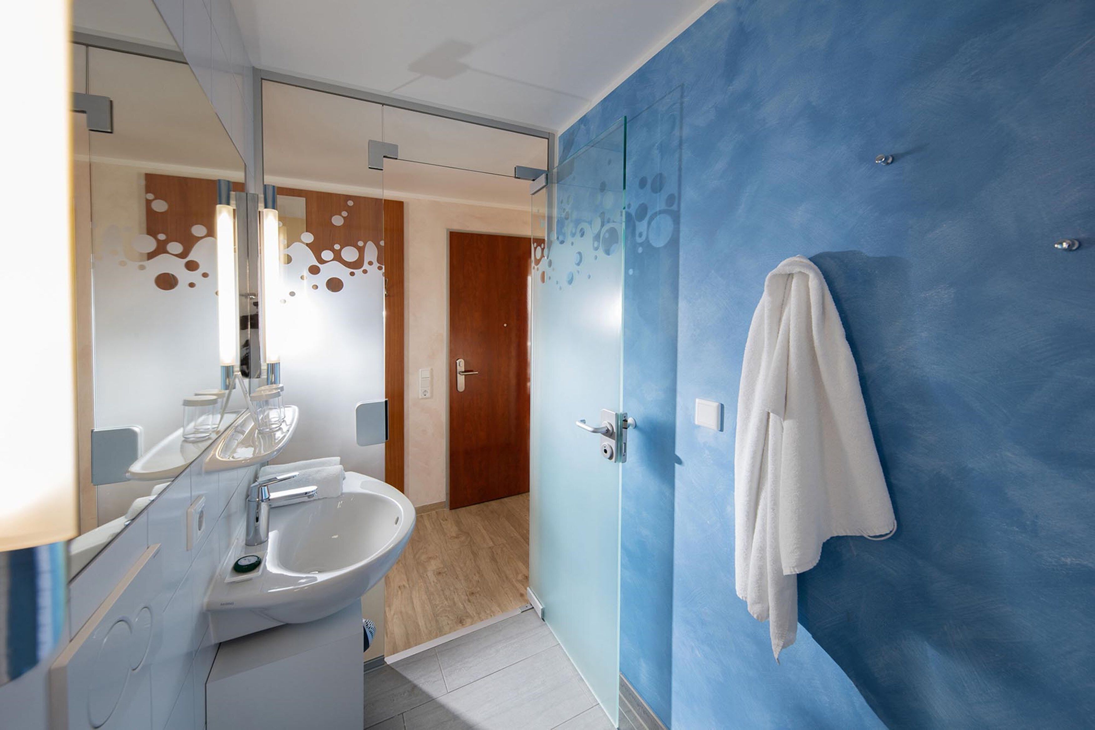 Casa de banho moderna com lavatório branco, espelho e parede azul.