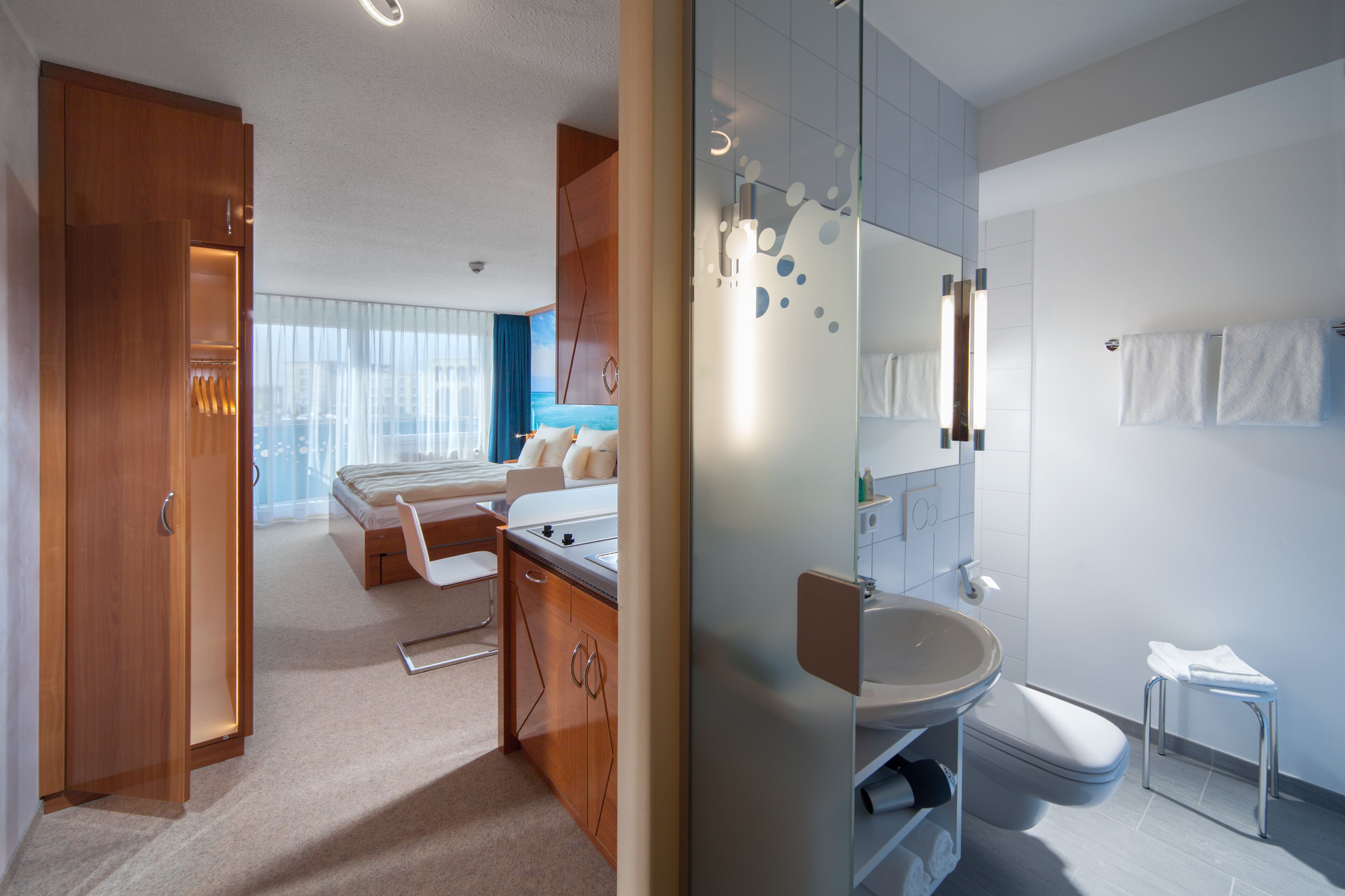 A modern hotel room with a bed, bedside table, and a bathroom with a sink and toilet.