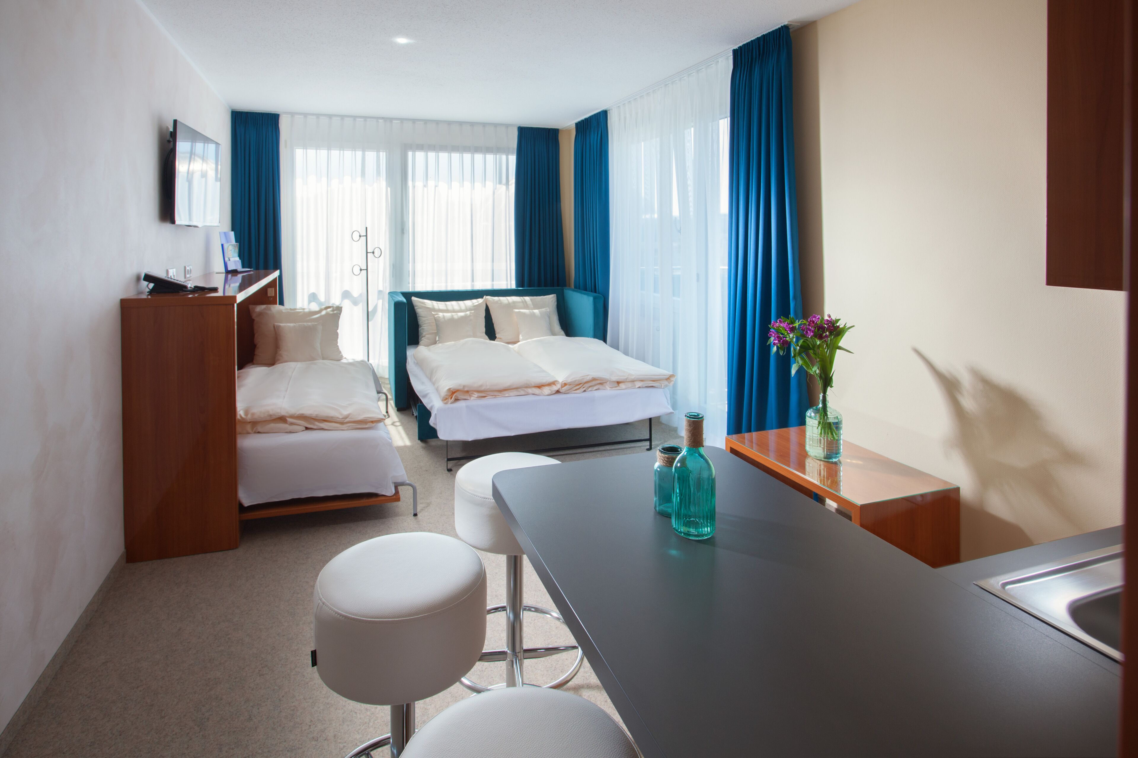 Una habitación de hotel con cama, escritorio, silla, mesita y televisor.