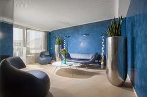 Un vestíbulo moderno con una pared azul de acento, un sofá de cuero, una mesa de centro redonda y una planta grande en maceta.