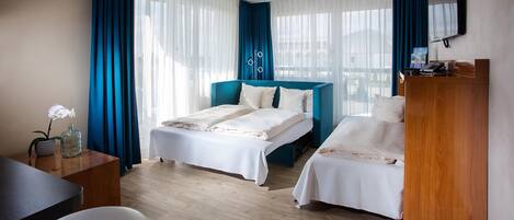 Une chambre d’hôtel avec deux lits, un bureau, une chaise, une télévision et une fenêtre avec des rideaux.