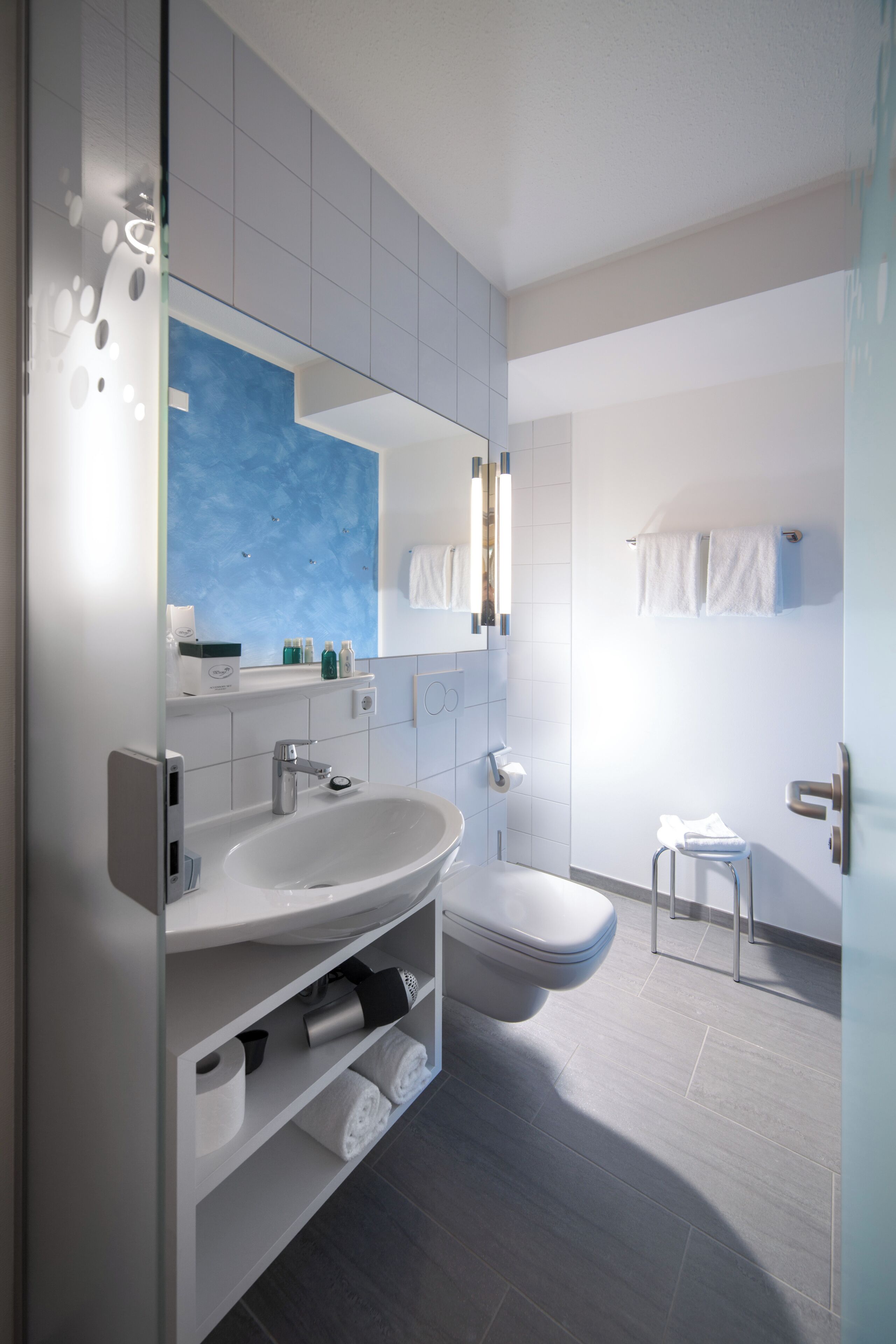 A modern bathroom with a large mirror, white sink, and a toilet.