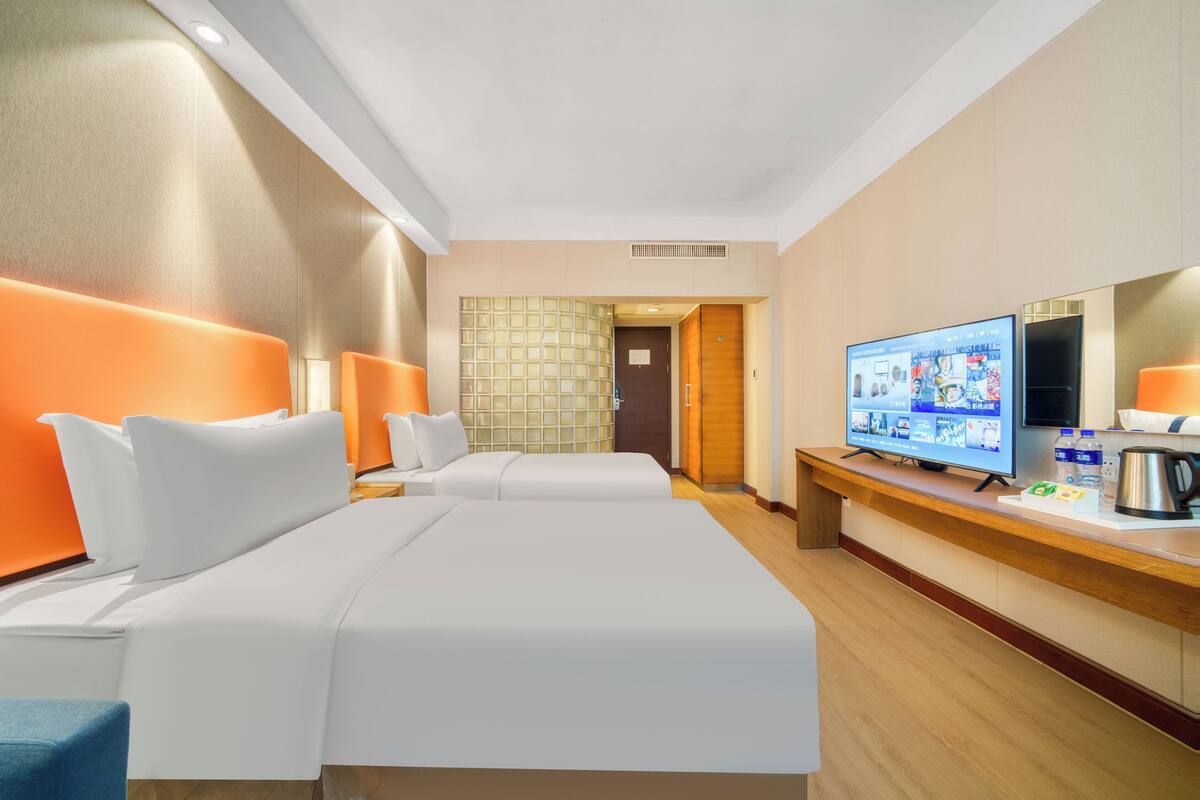 Ein Hotelzimmer mit zwei Betten, einem Fernseher, einem Schreibtisch mit Kaffeemaschine und einer Holztür.