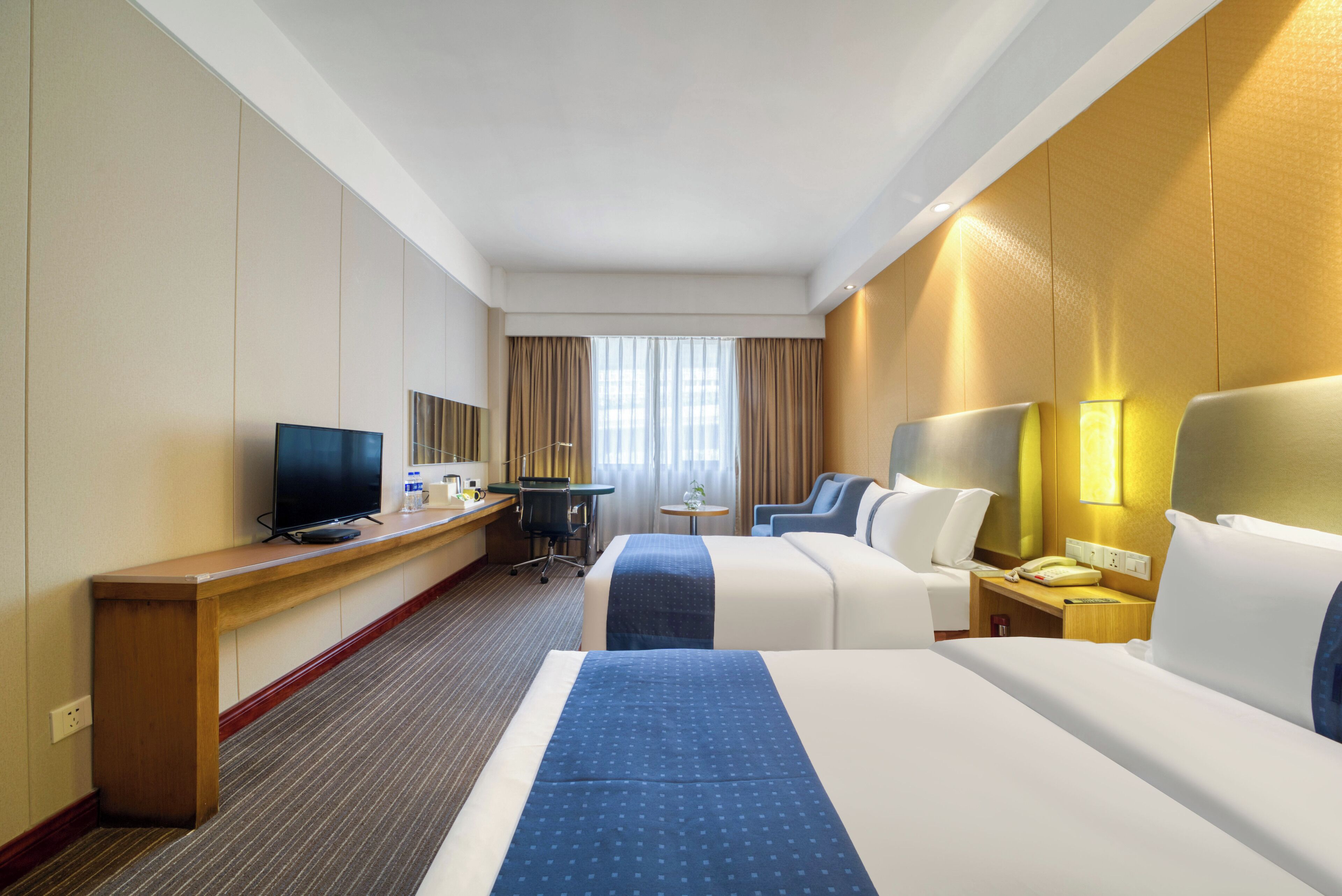 Une chambre d’hôtel avec deux lits, un bureau avec une télévision, une petite table et une chaise.