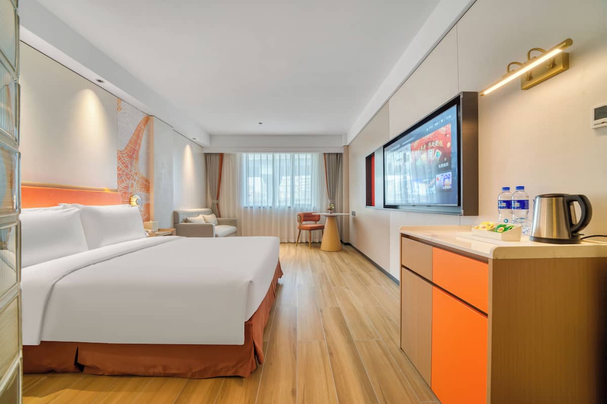 Ein Hotelzimmer mit einem großen Bett, einem Schreibtisch mit Wasserkocher und einem Fernseher.