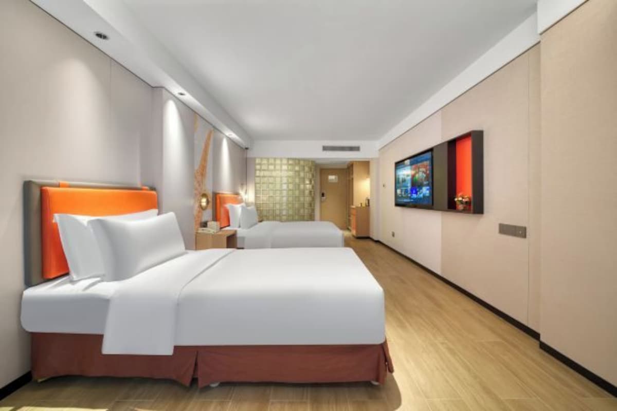 Habitación de hotel con dos camas, un televisor y un baño visible a través de una puerta abierta.