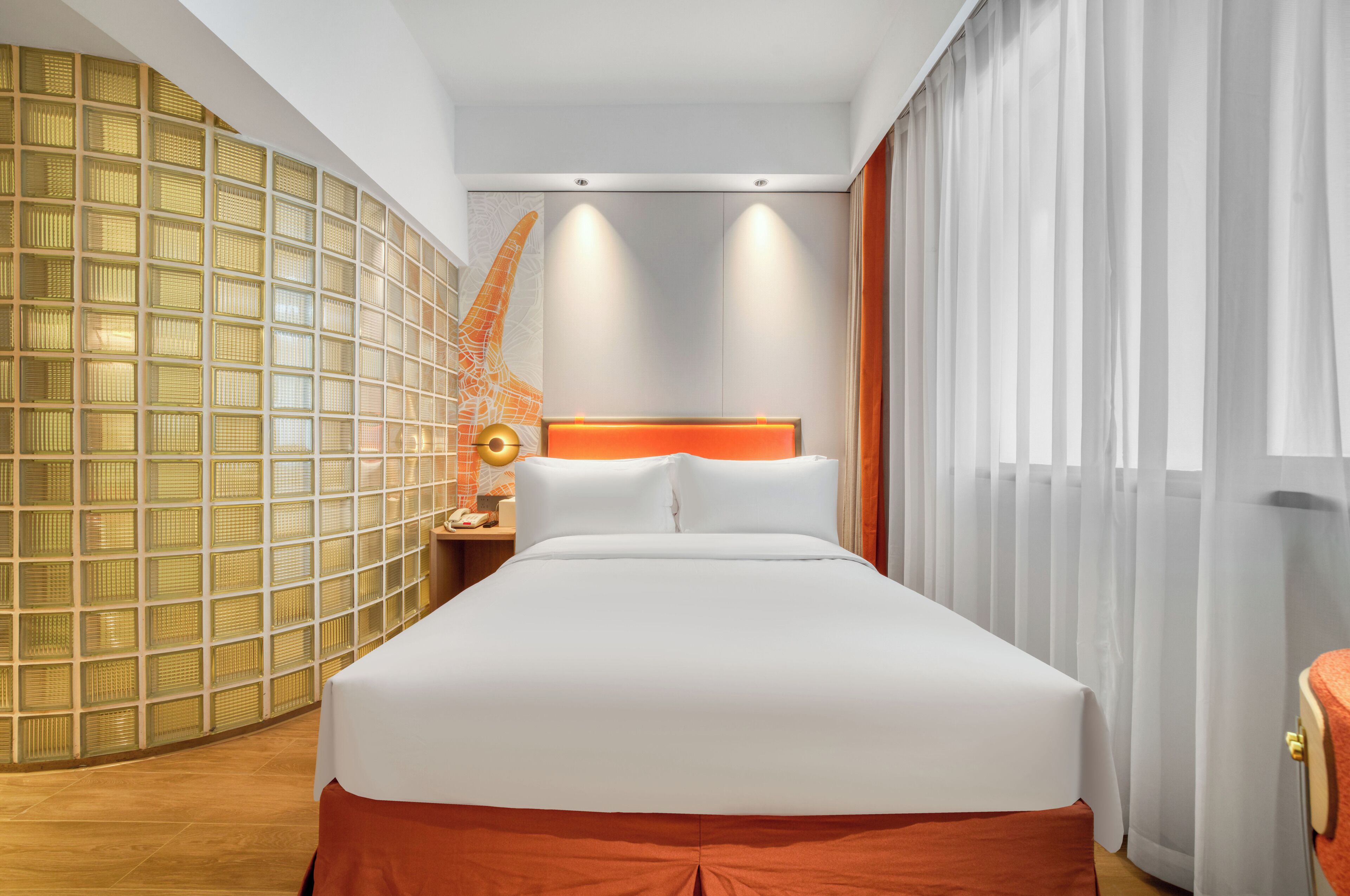 A hotel room with a large bed, a nightstand, a lamp, and a decorative wall with a geometric pattern.