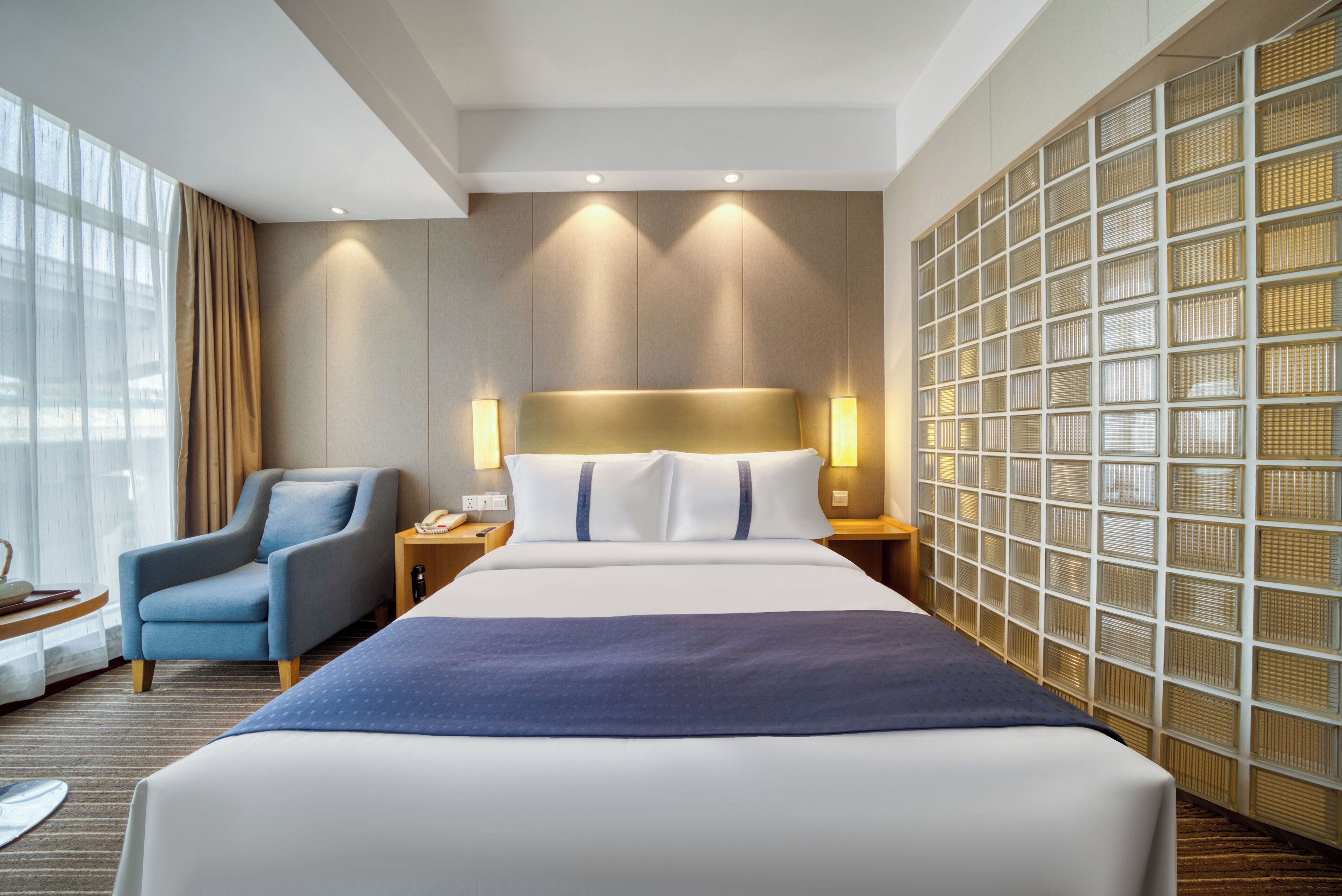 Une chambre d’hôtel moderne avec un grand lit, une chaise, une table de chevet et un mur orné d’un motif en quadrillage.