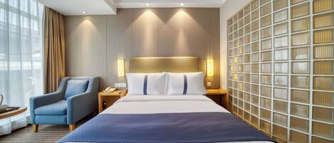 Ein modernes Hotelzimmer mit einem großen Bett, einem Sessel, einem Nachttisch und einer Wand mit Rasteroptik.