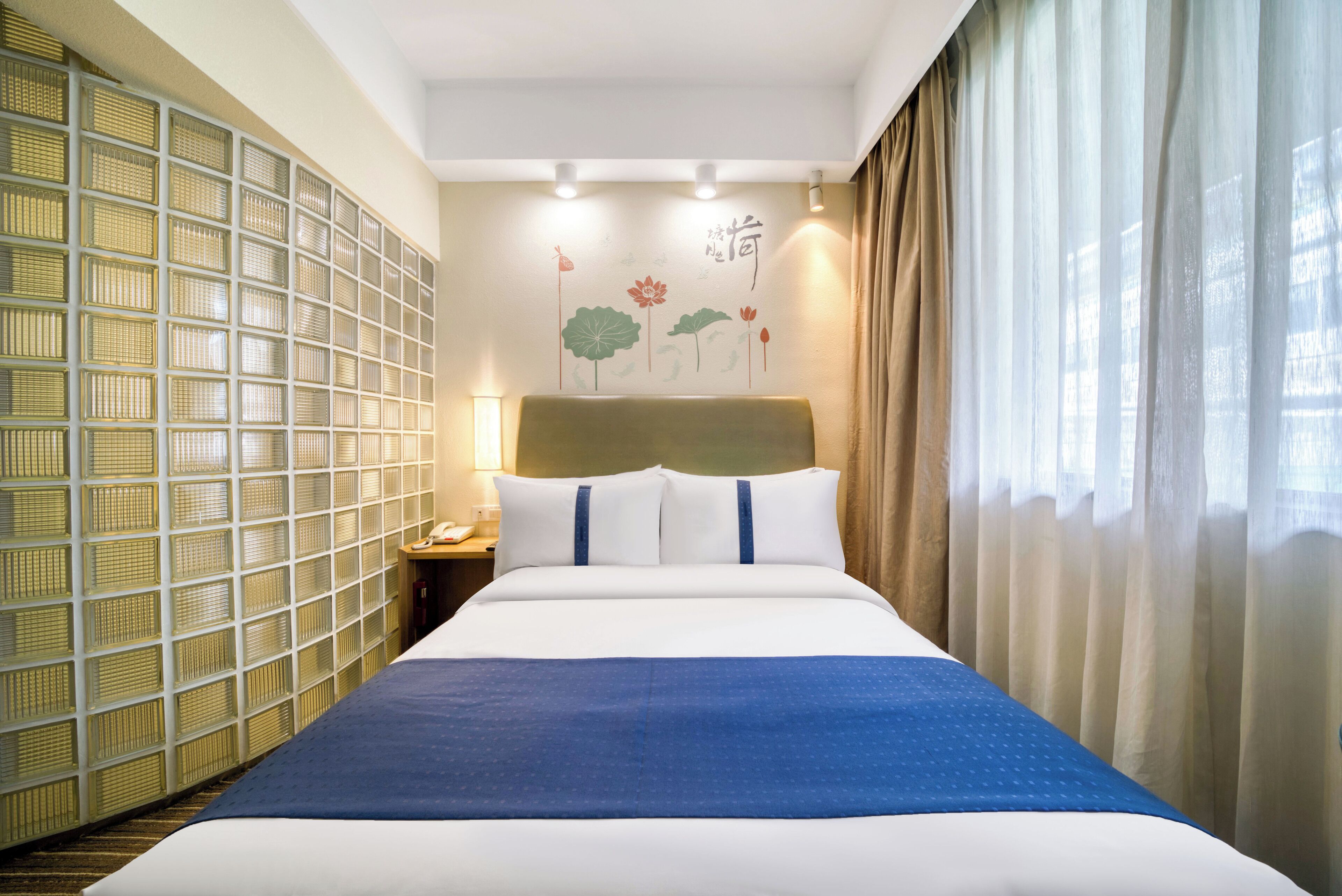 A hotel room with a large bed, a headboard, a nightstand with a lamp, and a wall with a decorative pattern.
