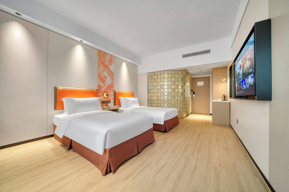 Ein Hotelzimmer mit zwei Betten, einem Fernseher und einem Badezimmer.