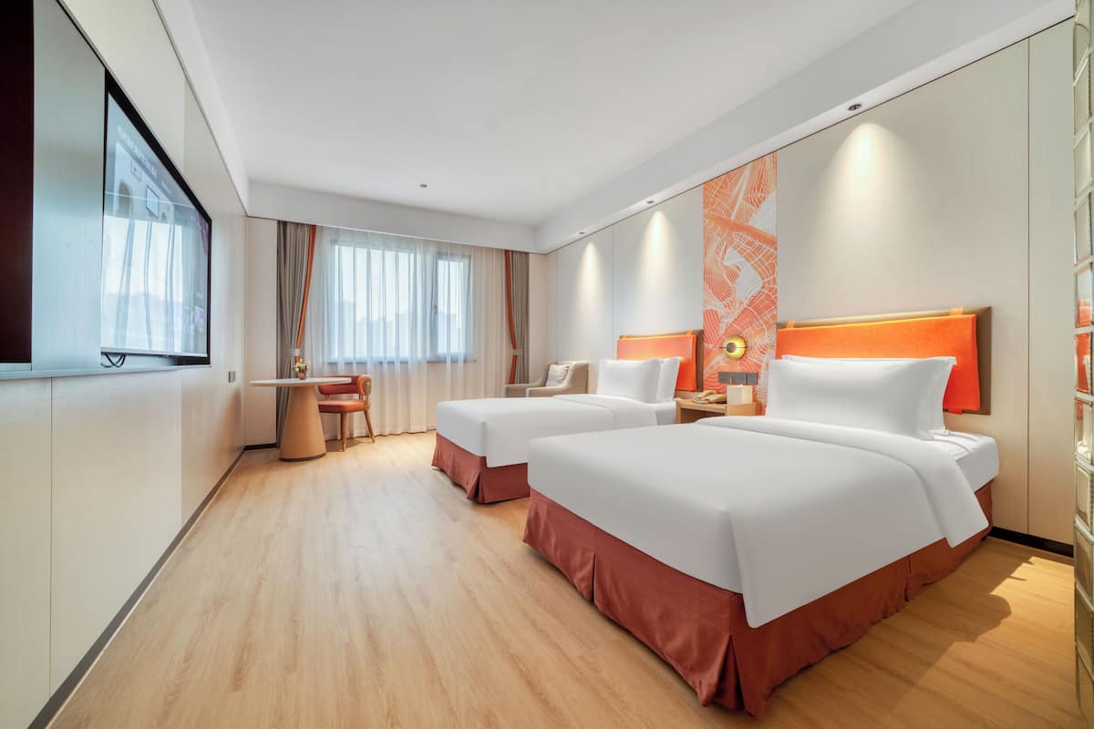 Ein Hotelzimmer mit zwei Betten, einem Schreibtisch und einem Fernseher.