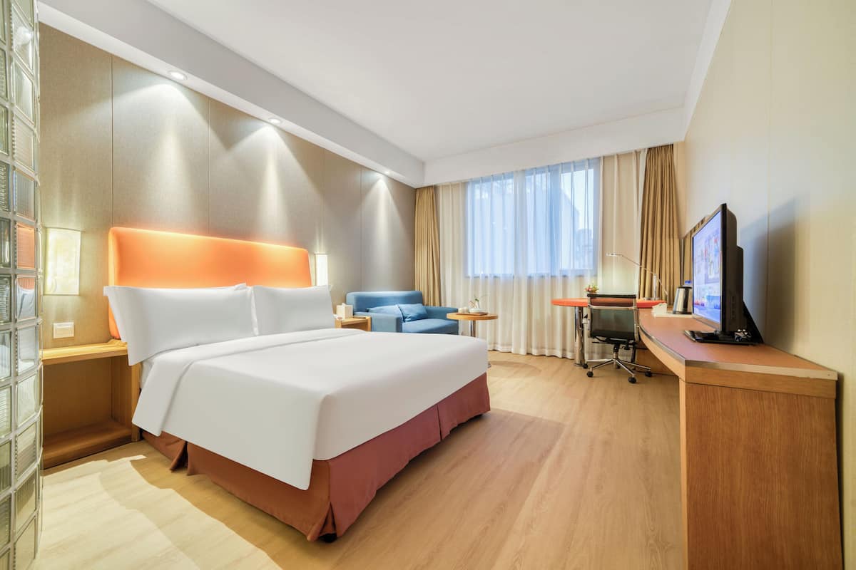 Ein Hotelzimmer mit einem großen Bett, einem Schreibtisch mit Computer, einem Sessel und einem Fernseher.