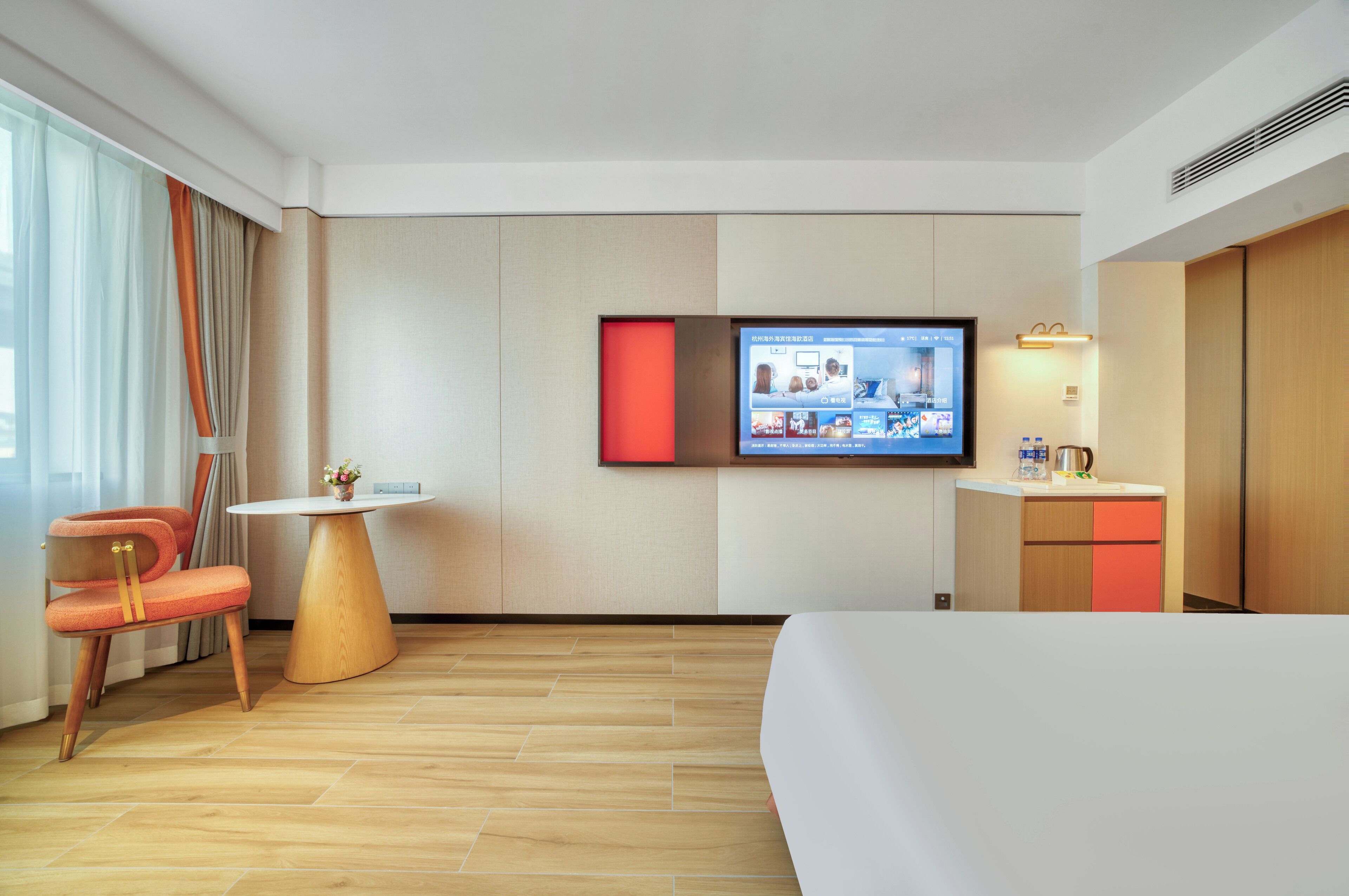 A hotel room with a bed, a TV mounted on the wall, a small round table, a chair, and a cabinet.