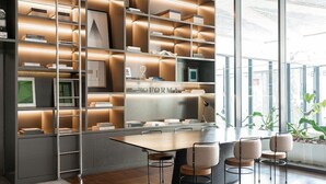 A modern office space with a large wooden table, multiple chairs, and a bookshelf with various items. - Forma Itaim by Q Apartments (São Paulo)