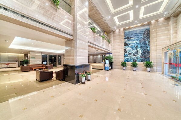 A spacious lobby with a high ceiling, marble flooring, a reception desk, seating area, and a large painting. - Hangzhou Haiwaihai Nachuan Hotel (Hangzhou)