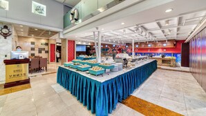 Disposição de buffet com uma mesa comprida, um balcão de recepção e teto alto com vigas aparentes.