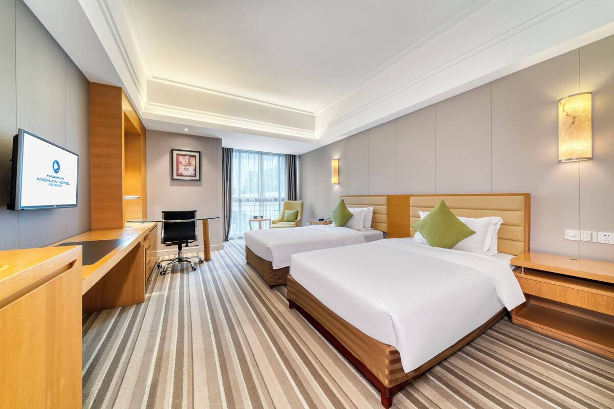 Ein Hotelzimmer mit zwei Betten, einem Schreibtisch, einem Stuhl, einem Fernseher und einem großen Fenster.