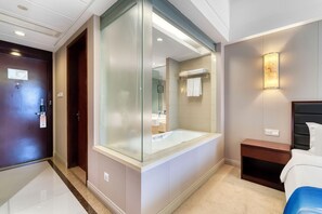 A modern hotel room with a glass-enclosed shower, a large bathtub, a bedside table, and a bed with a headboard. - Hangzhou Haiwaihai Nachuan Hotel (Hangzhou)