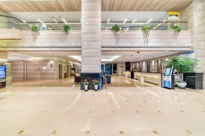 Un vestíbulo amplio con techo alto, una mesa de recepción y plantas en macetas.
