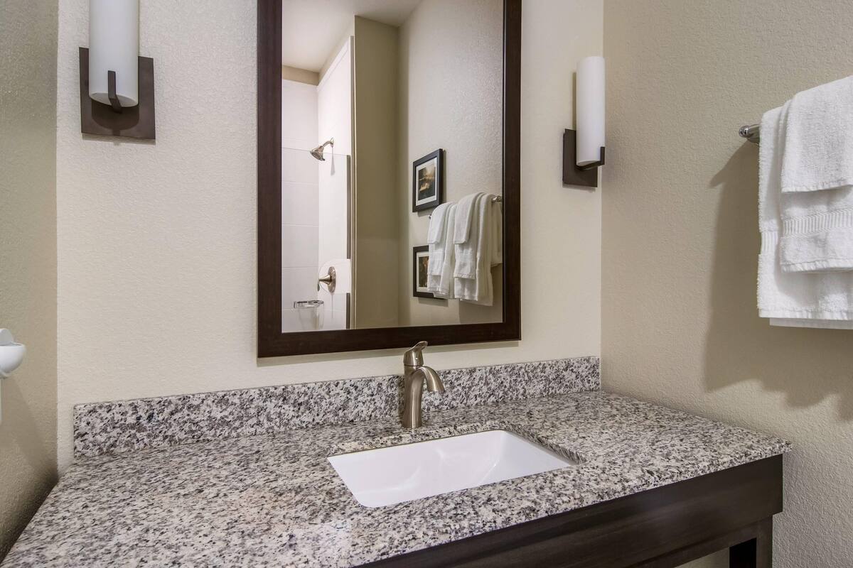 A bathroom with a granite countertop, a white sink, a large mirror, and two wall-mounted towel racks.