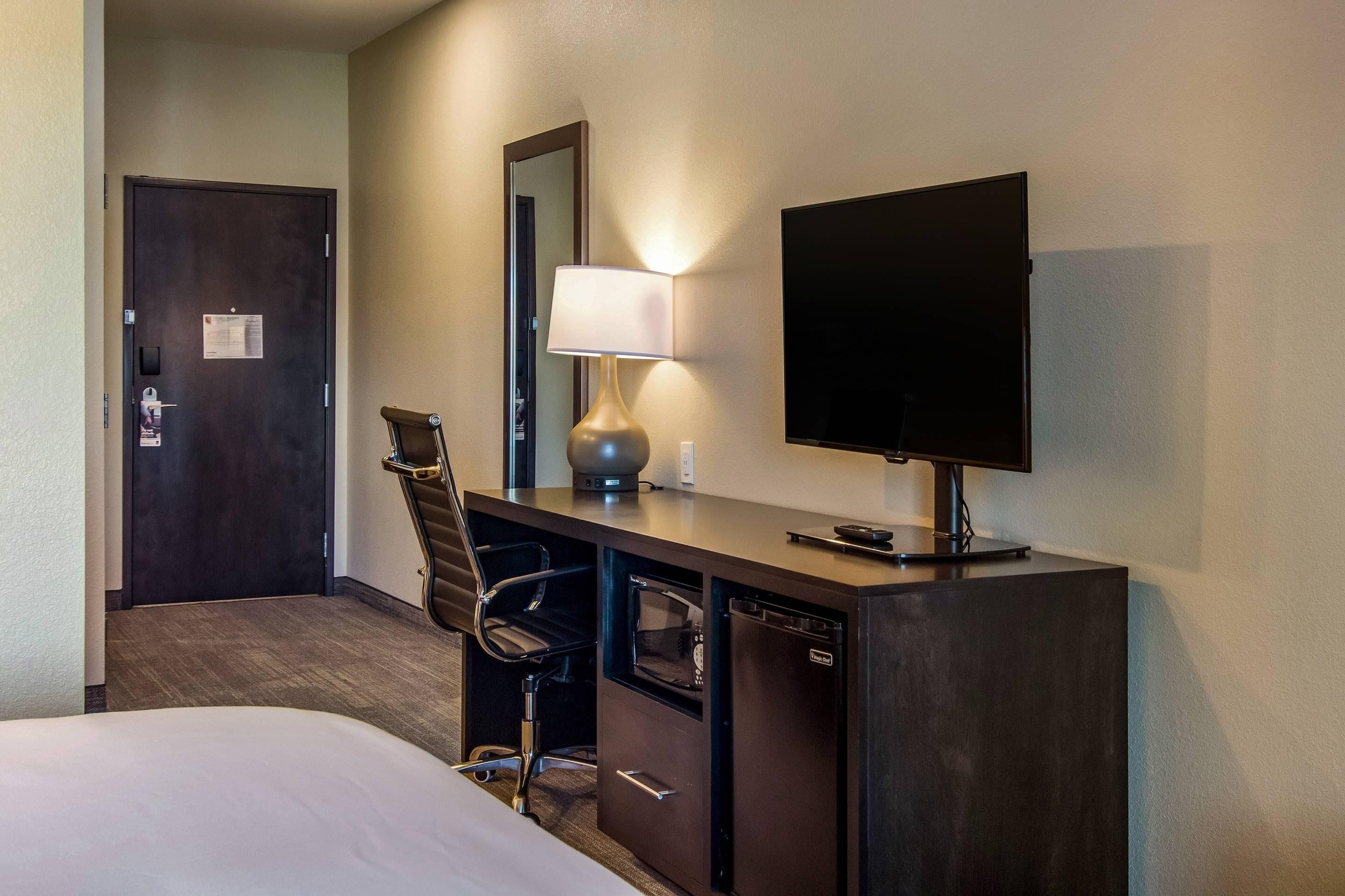 A hotel room with a bed, a desk with a lamp, a television, and a chair.