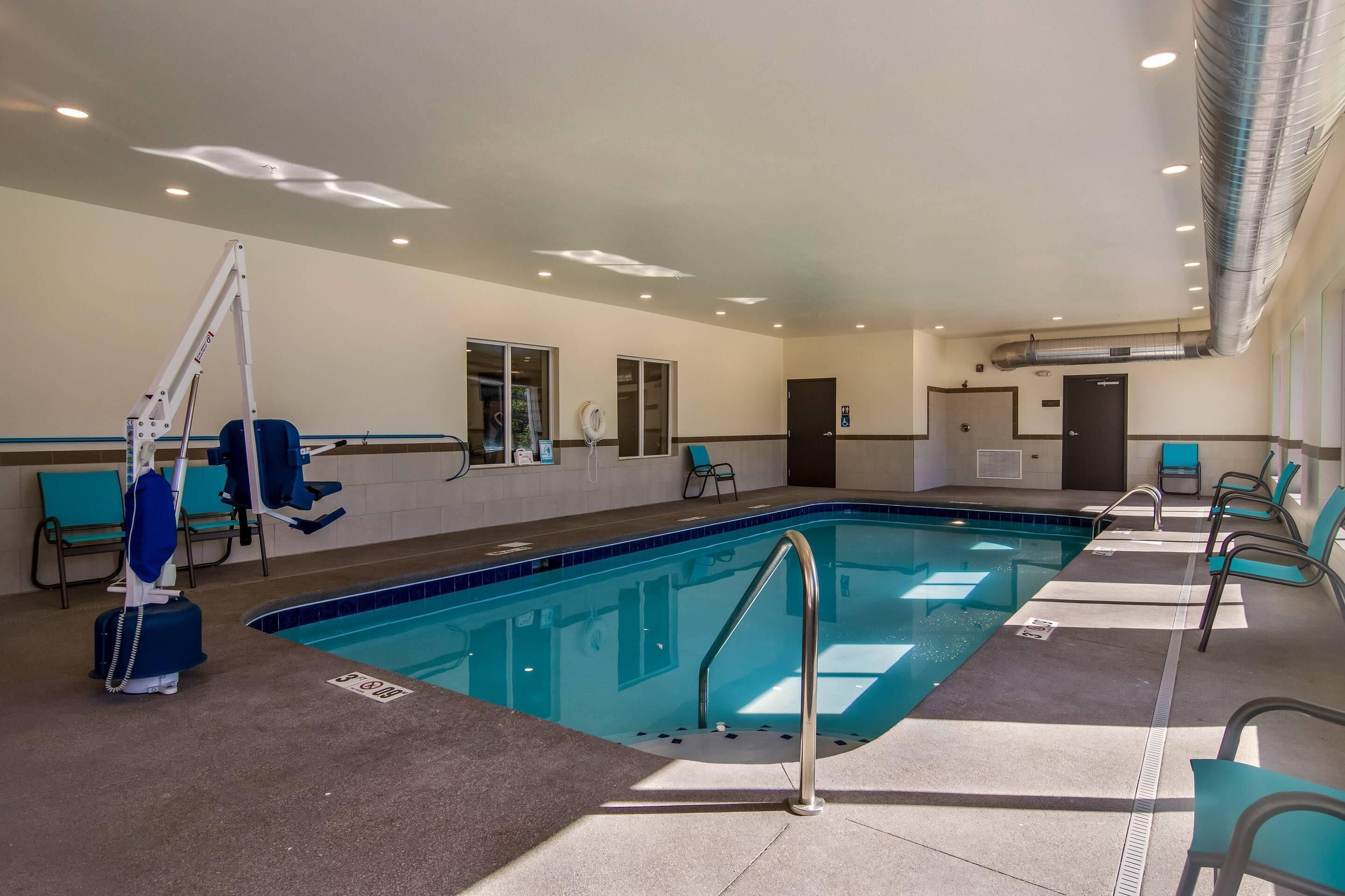 An indoor swimming pool with clear lanes, a lifeguard stand, and seating along the sides.