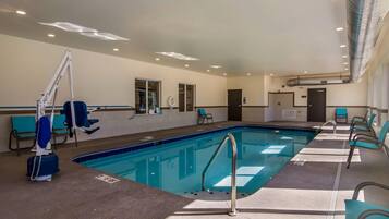An indoor swimming pool with clear lanes, a lifeguard stand, and seating along the sides.