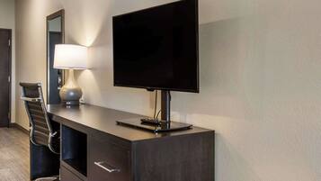 Habitación de hotel con un escritorio de madera oscura, un televisor de pantalla plana, una lámpara y una silla.