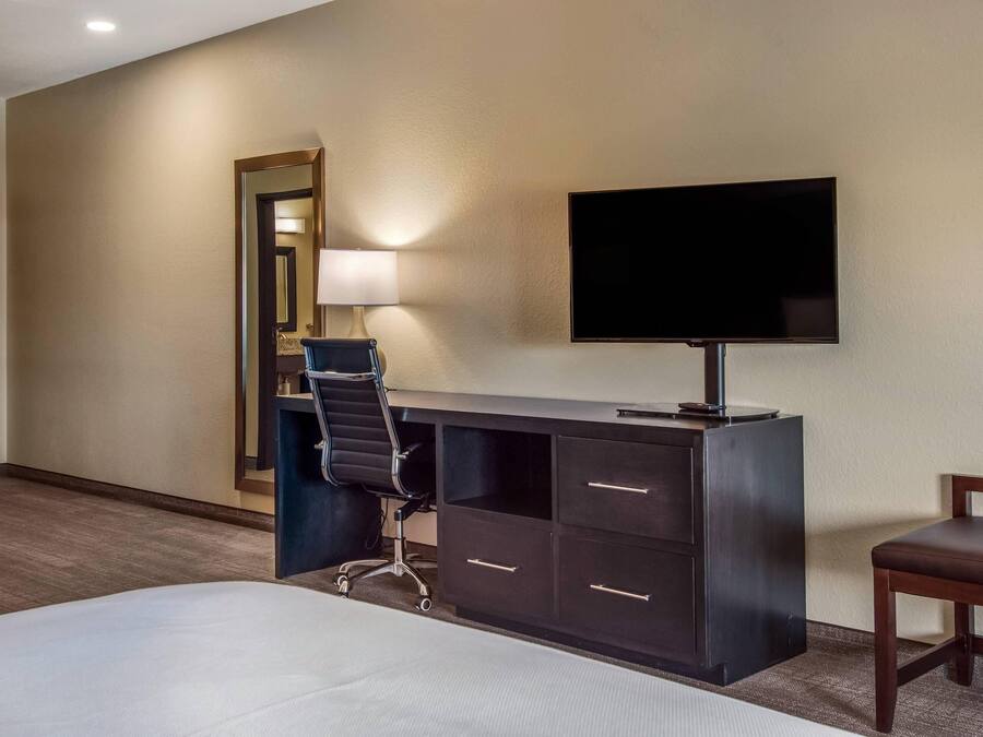 Una habitación de hotel con cama, escritorio, silla, televisor y espejo.