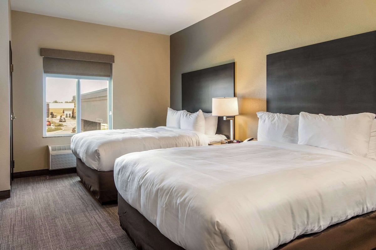 A hotel room with two beds, a large window, and a view of the outside.
