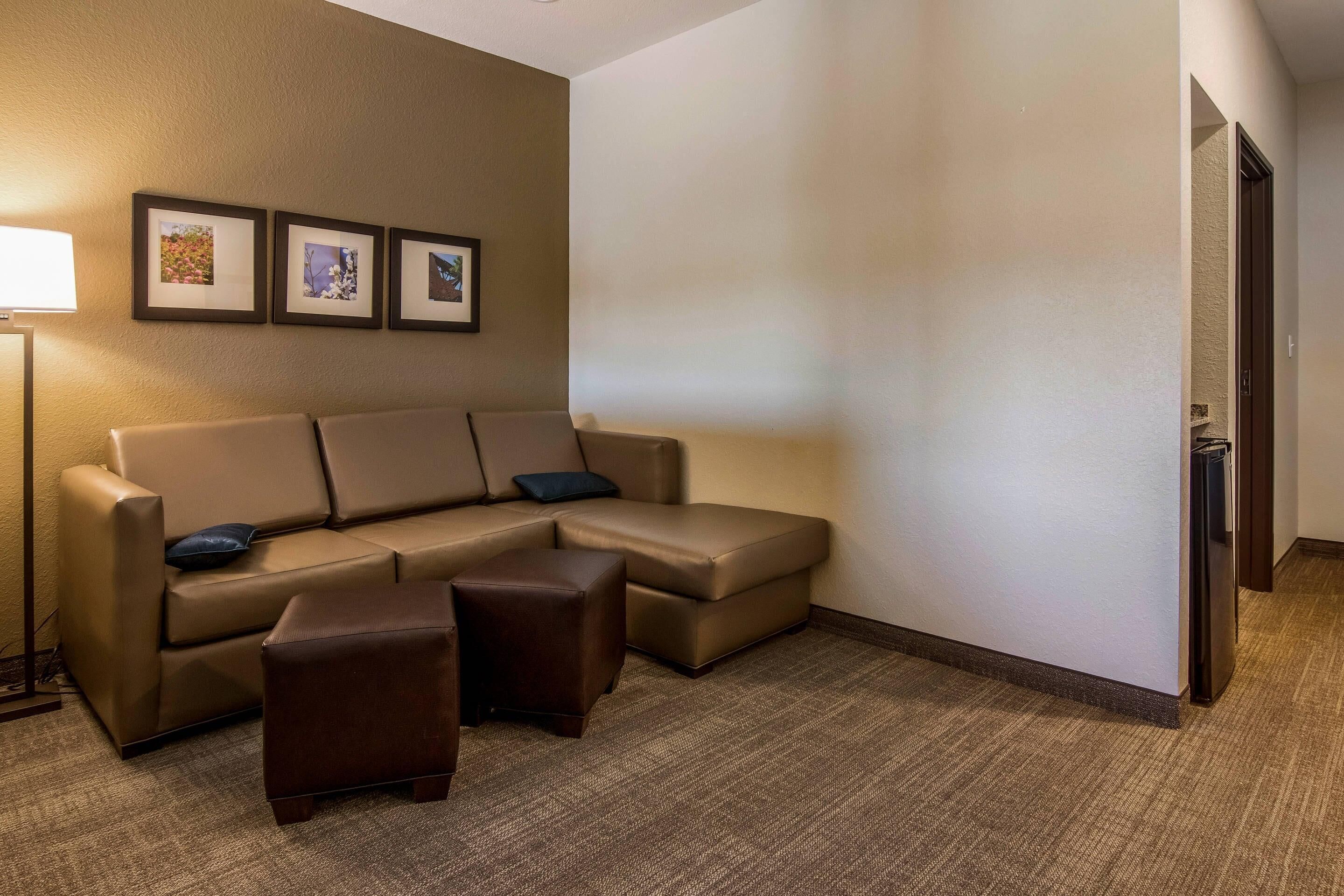 A hotel room with a beige sectional sofa, a small ottoman, and three framed pictures on the wall.