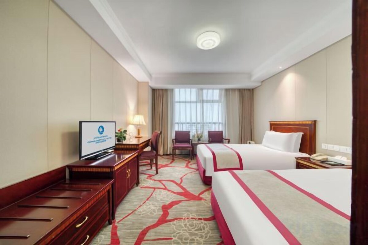 Una habitación de hotel con una cama, un escritorio con televisor, una silla y una ventana con cortinas.