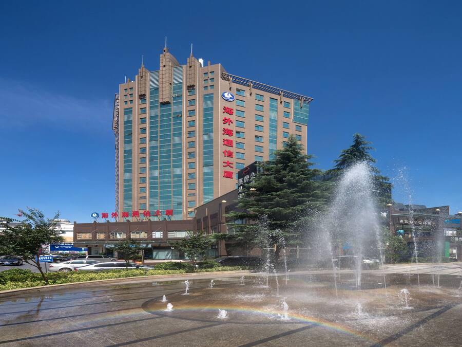Um hotel alto com design moderno, uma fonte em primeiro plano e um céu azul límpido.