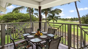 A covered outdoor dining area with a table set for four, overlooking a well-maintained lawn and palm trees. - Waikoloa Beach S P32 2 Bedroom Villa by RedAwning (Waikoloa)