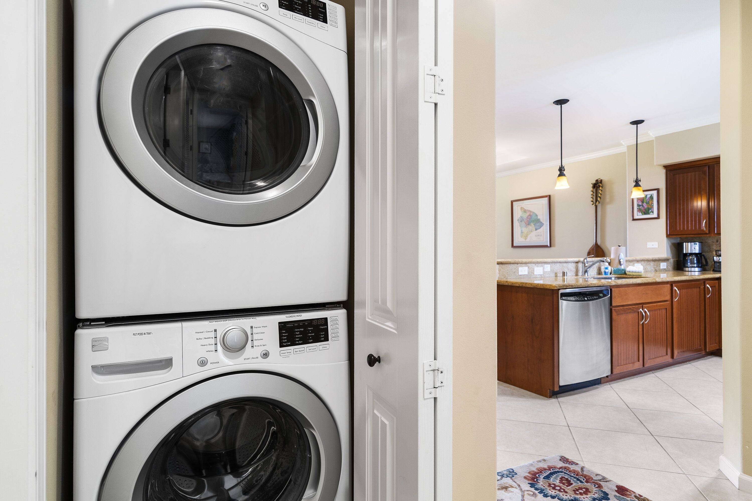 A laundry area with stacked washers and dryers, a kitchen with wooden cabinets and a dishwasher, and pendant lighting.