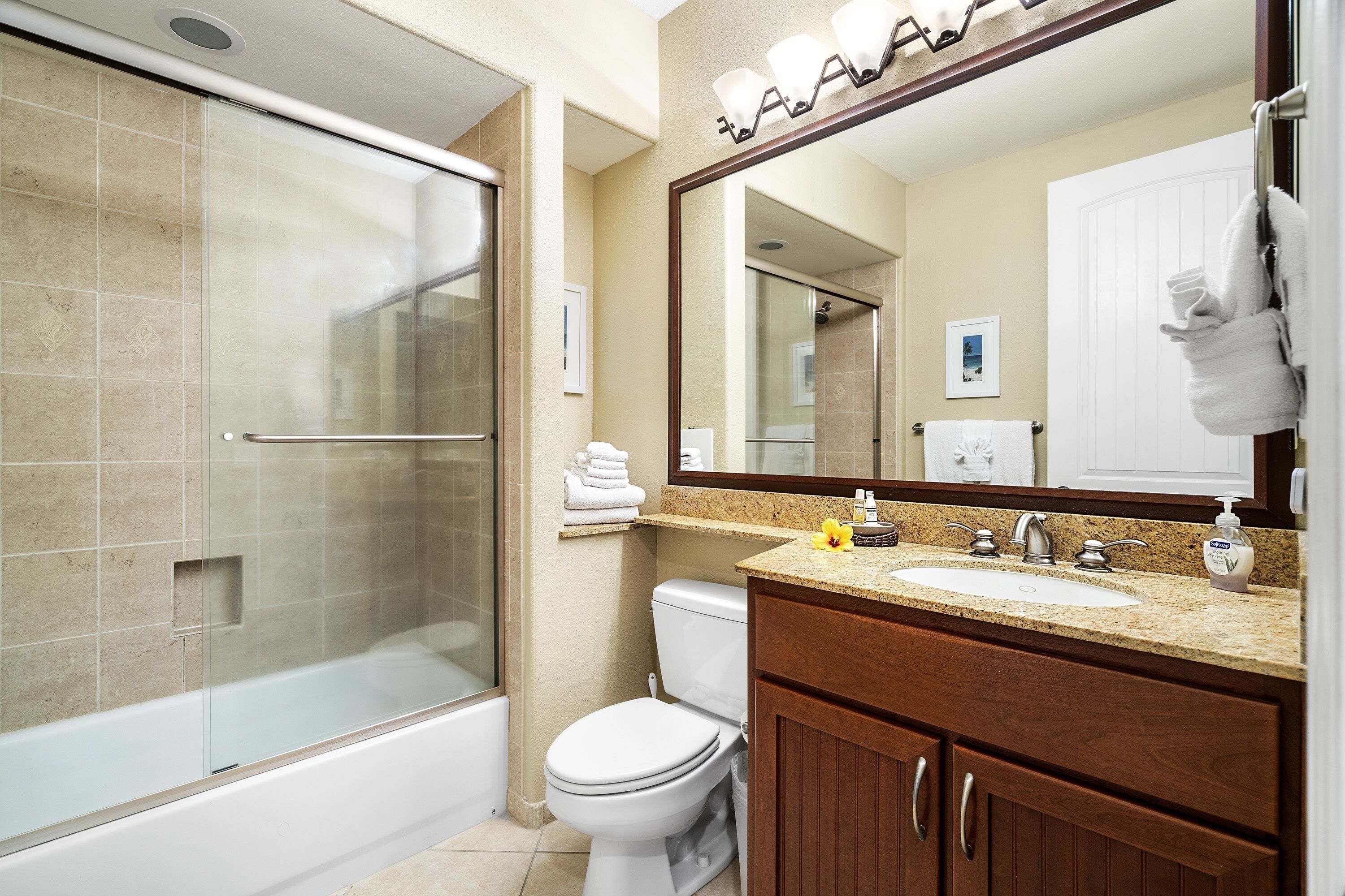 A modern bathroom with a glass-enclosed shower, a white toilet, a sink with a mirror above, and wooden cabinets.