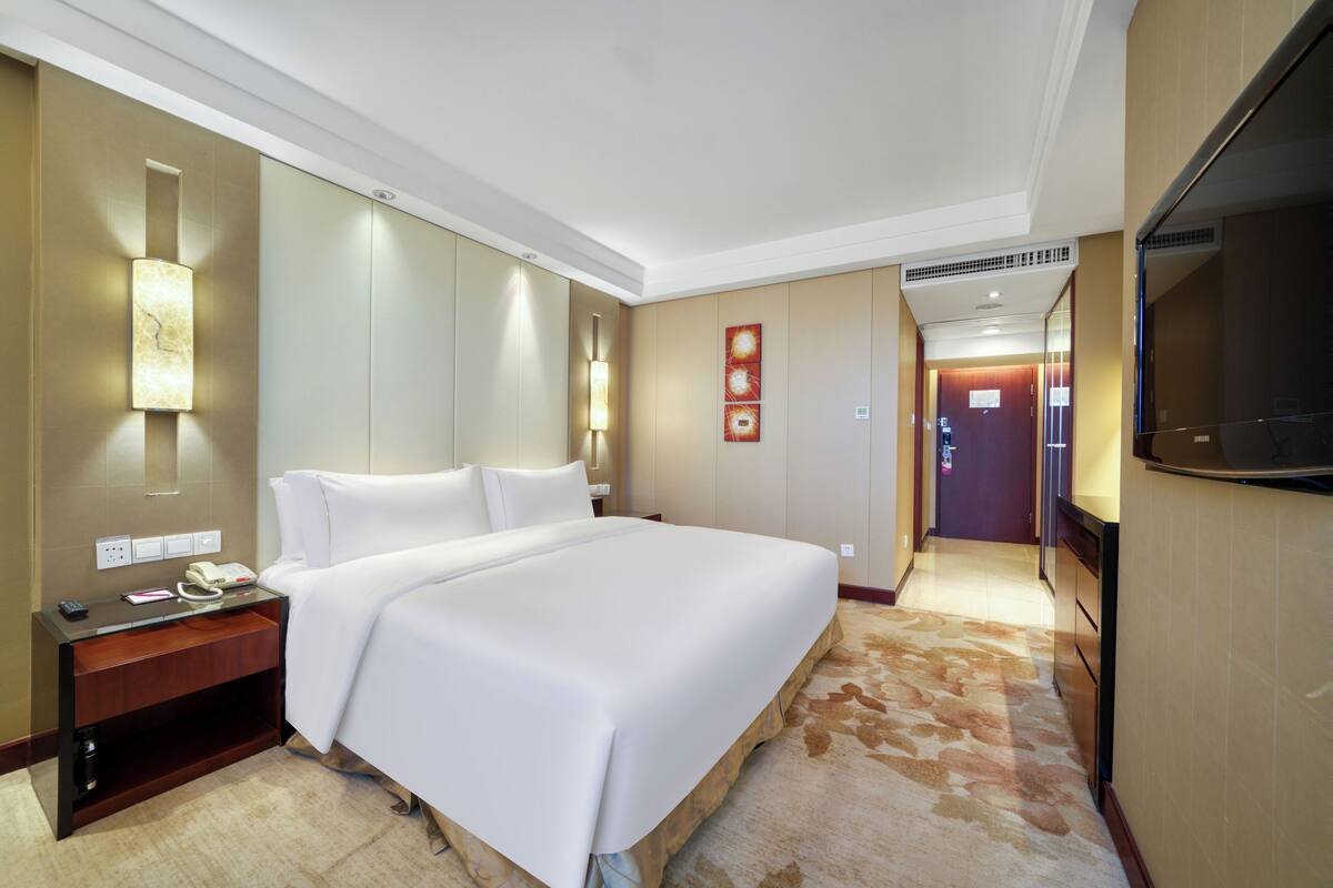 A hotel room with a large bed, bedside table with a phone, and a TV.